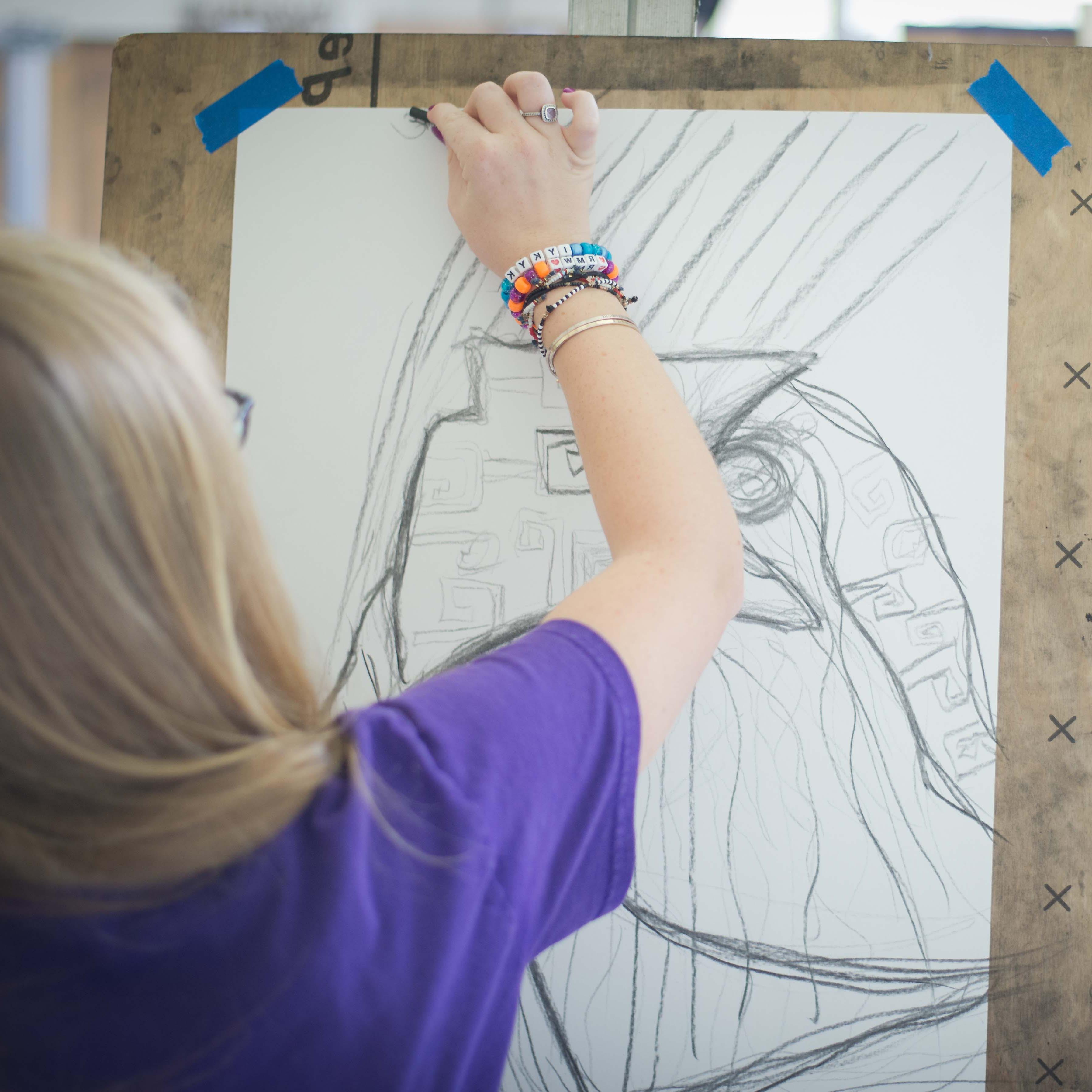 A student sketches on paper taped to an easel